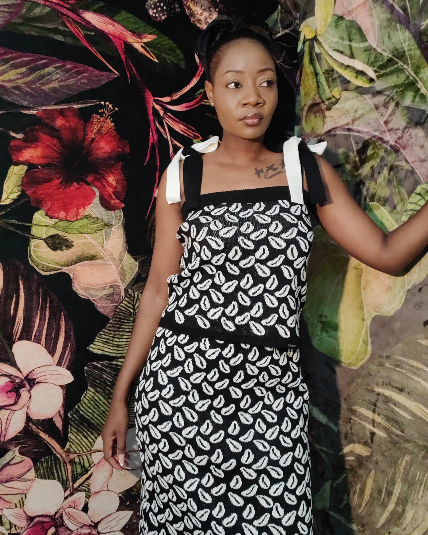 Woman wearing a black and white patterned dress against a colorful floral and leaf background