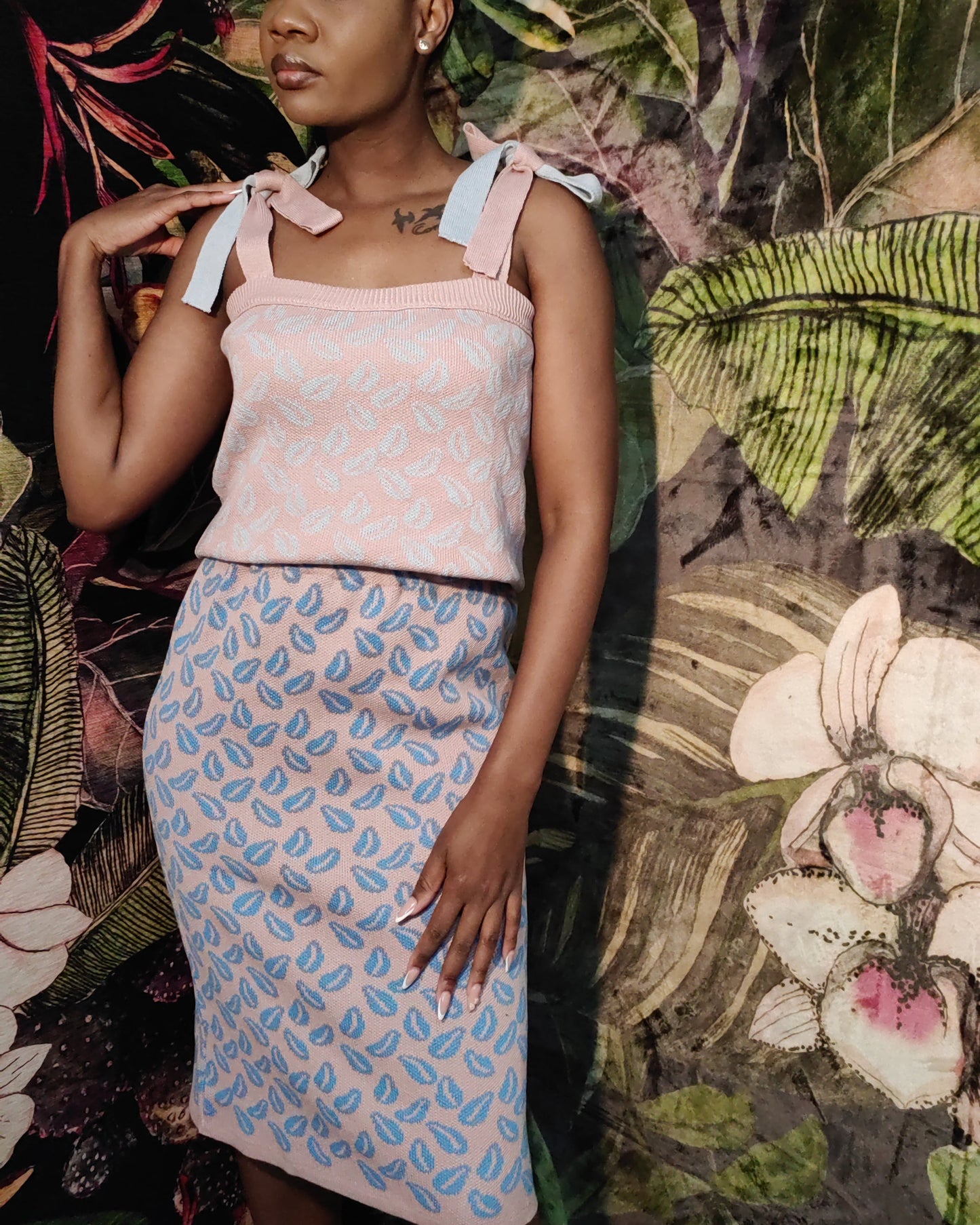Woman wearing a patterned top and skirt against a floral and leafy background