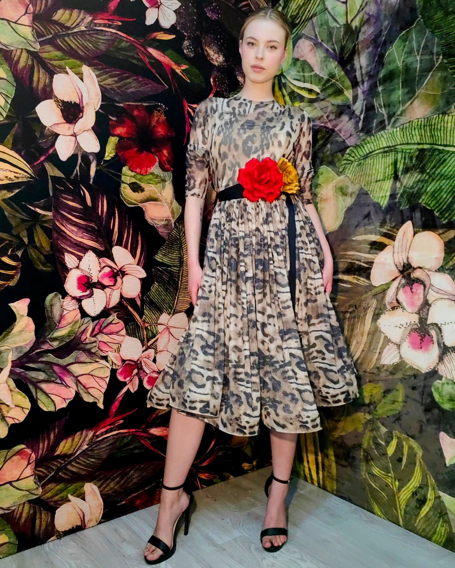 Model wearing a patterned dress with a red flower against a floral backdrop