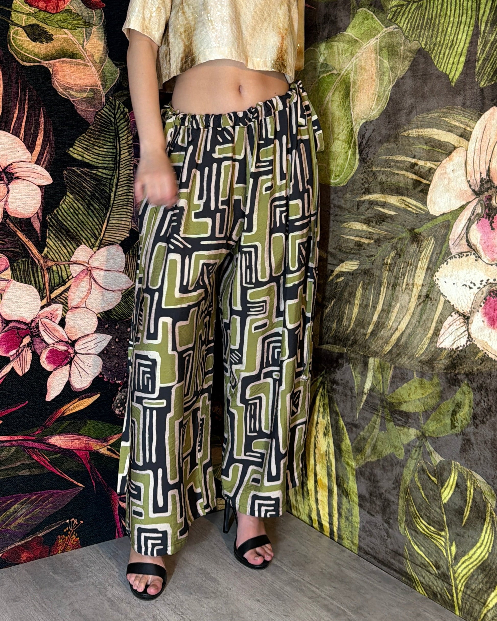 Woman wearing a patterned outfit standing against a floral and leafy background