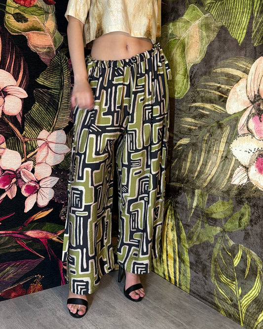 Woman wearing a patterned outfit standing against a floral and leafy background