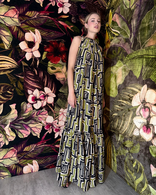 Woman in a patterned dress standing against a vibrant floral and nature-themed wall.