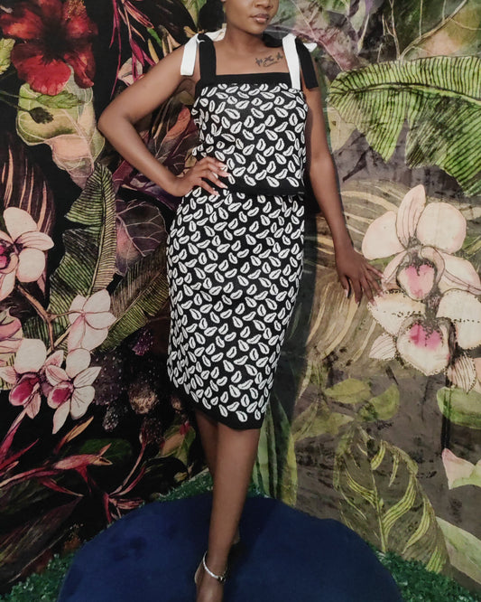Woman in a black and white patterned dress standing against a colorful floral and leaf background.