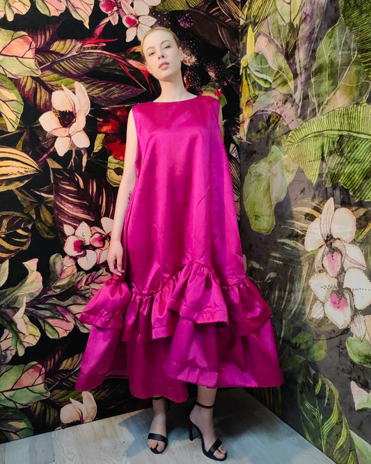 Woman wearing a bright pink dress standing against a floral and leaf-patterned wall.