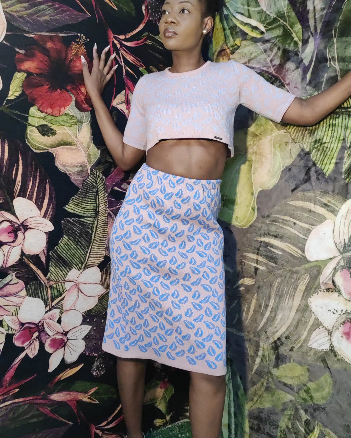 Woman posing in front of a colorful floral and leaf patterned wall.