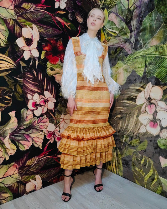 Woman in a striped dress with a white shawl against a floral and leaf-patterned wall.