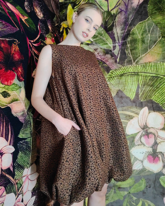 Woman wearing a brown patterned dress against a colorful floral and leaf background