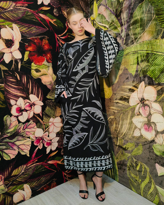 Woman in a black and white patterned dress standing against a floral and leafy background