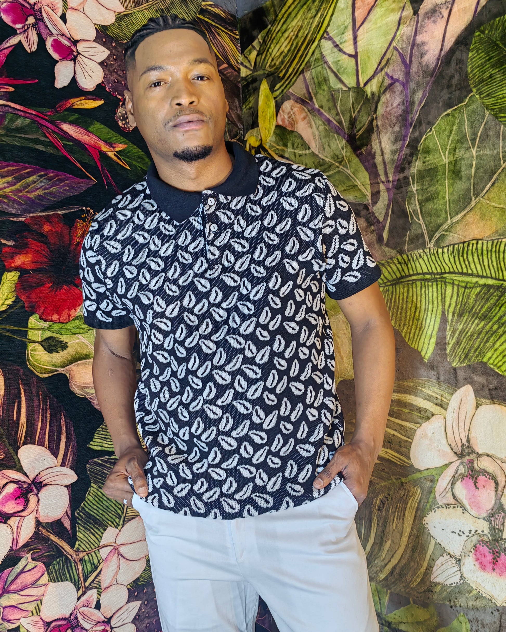 Man wearing a black and white patterned shirt against a colorful floral and leaf background