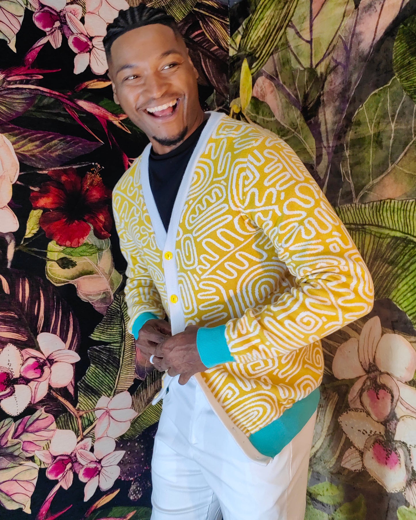 Man wearing a yellow patterned cardigan standing against a floral background