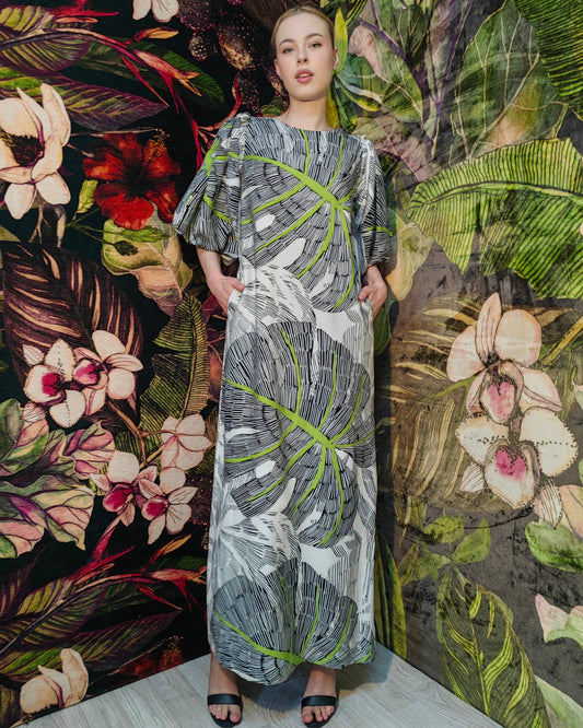 Woman in a patterned dress standing against a floral and leafy textured wall.