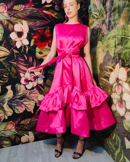 Model wearing a bright pink dress with ruffled layers against a floral background