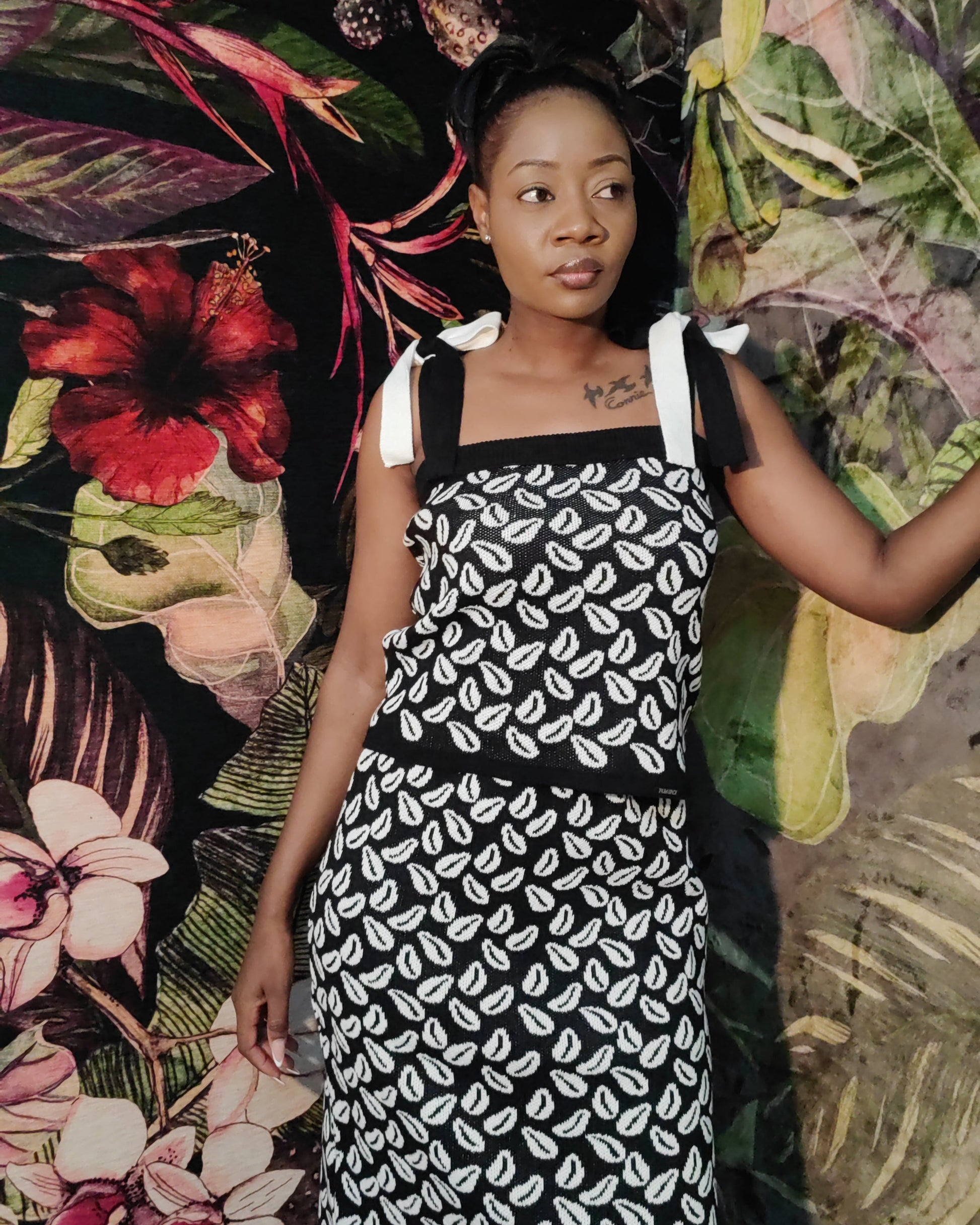 Woman wearing a black and white patterned dress against a colorful floral and leaf background