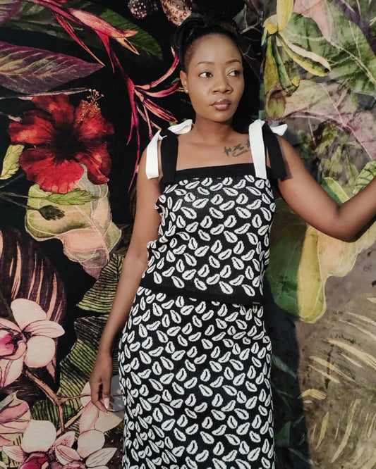 Woman wearing a black and white patterned dress against a colorful floral and leaf background