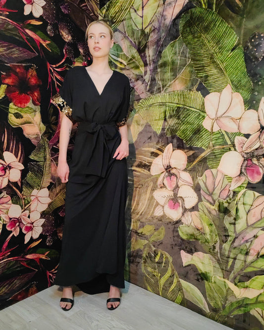 Woman in a black dress standing against a floral and nature-themed wall.