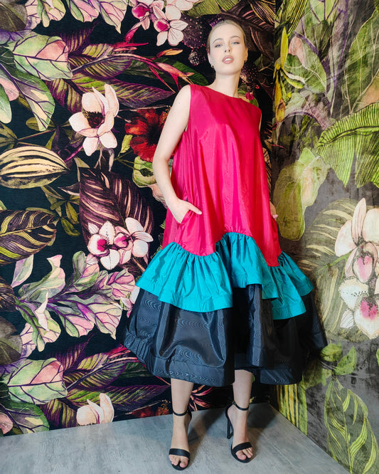 Woman wearing a colorful dress with a vibrant floral and leaf patterned wall behind her