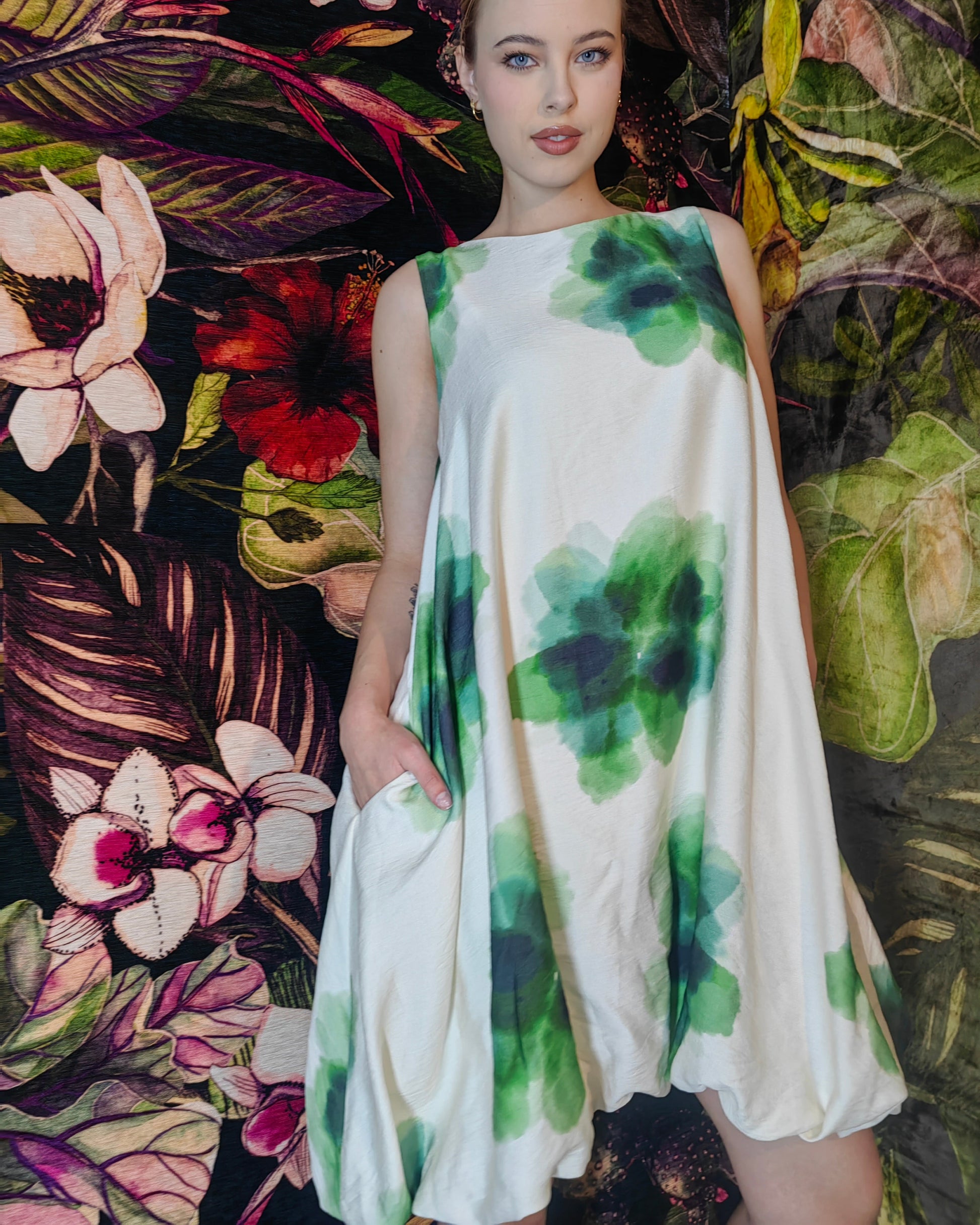 Woman wearing a white dress with green floral patterns against a colorful floral background
