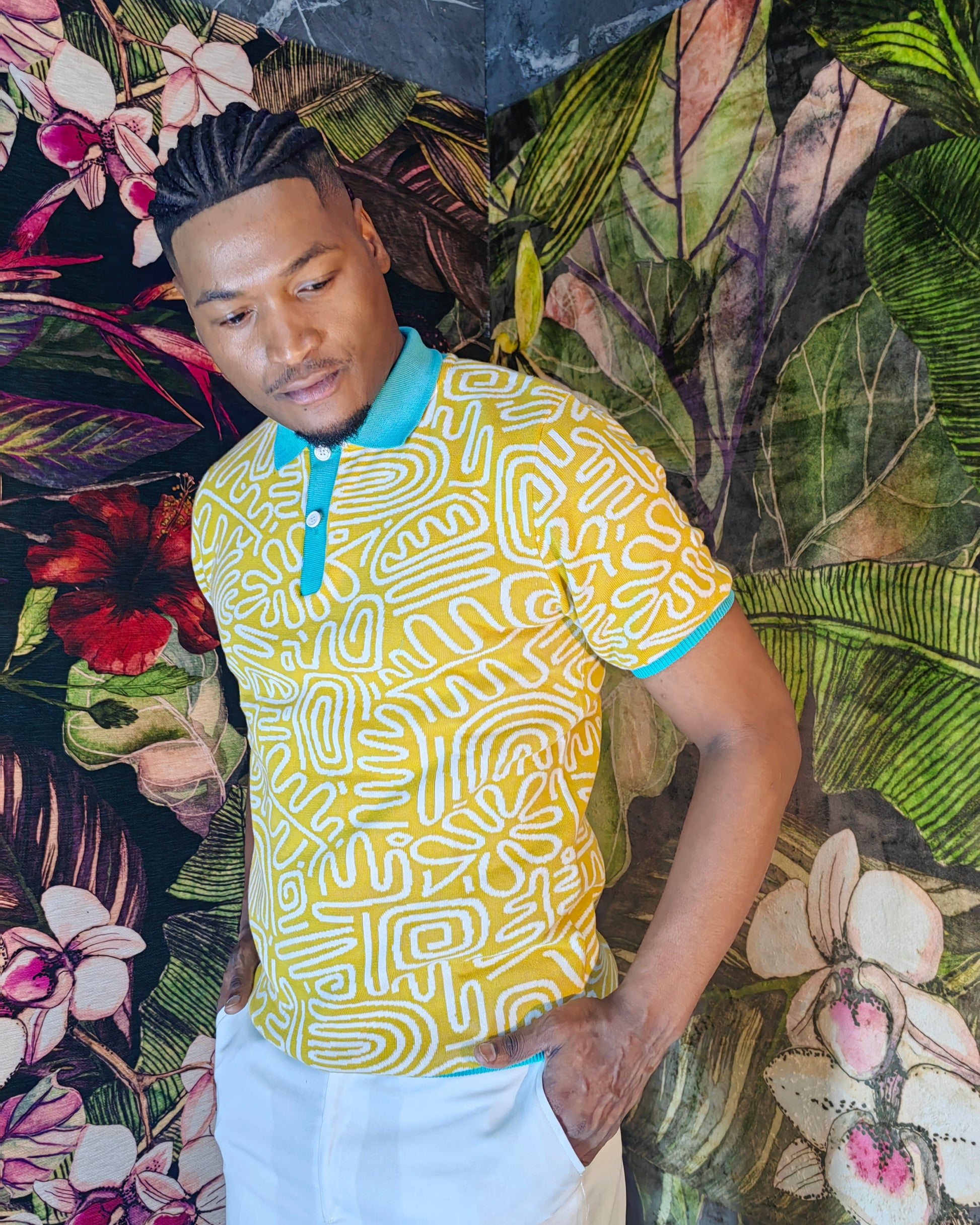 Man wearing a yellow patterned shirt standing against a tropical leaf background