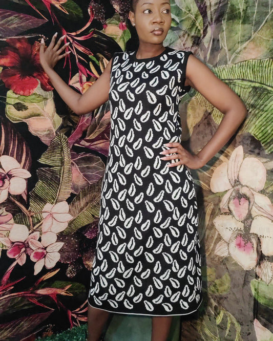 Woman in a black and white patterned dress standing against a colorful floral and leaf background