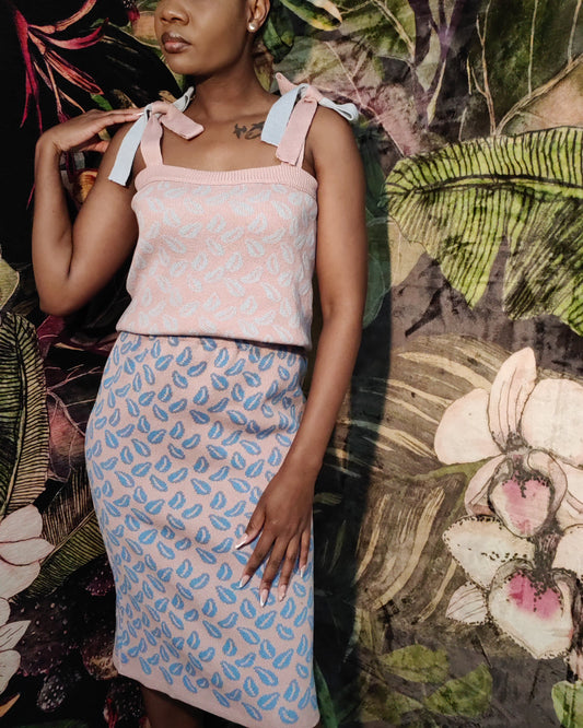 Woman wearing a patterned top and skirt against a floral and leafy background