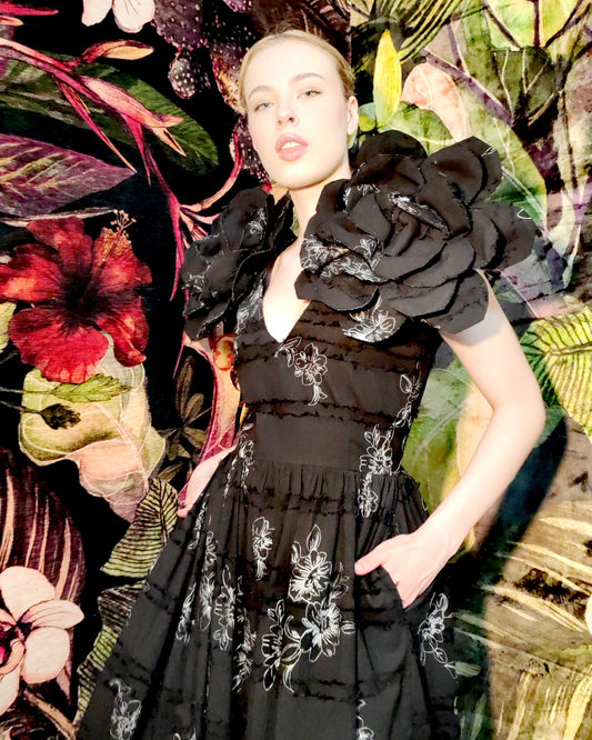 Woman in a black floral dress standing against a colorful floral background