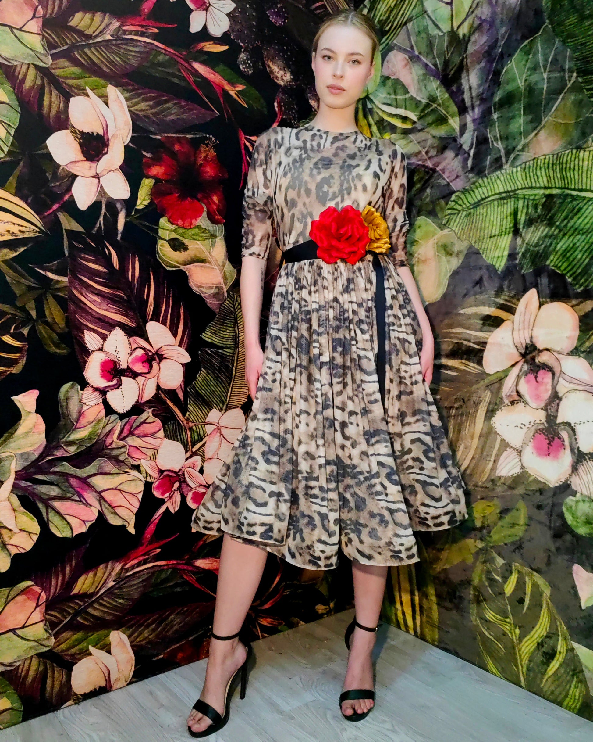 Model wearing a patterned dress with a red flower against a floral backdrop