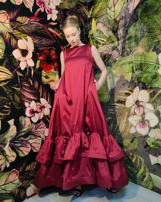 Woman in a red dress standing against a floral and leaf-patterned wall.