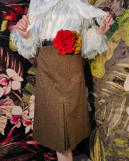 Person wearing a brown skirt with a floral top and white ruffled sleeves against a floral background