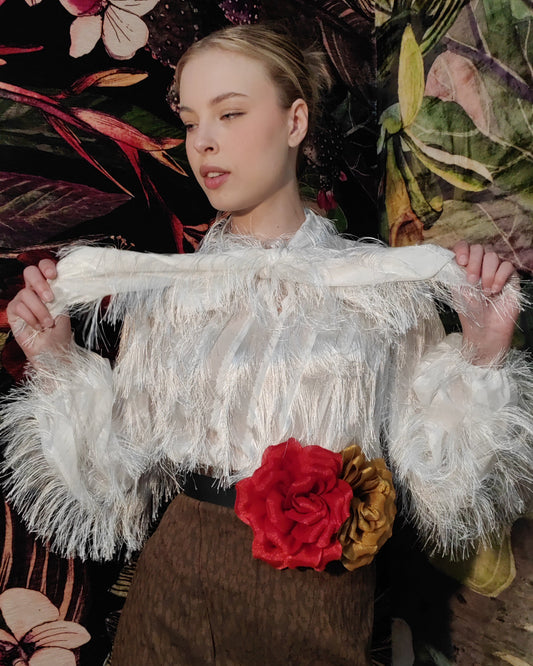 Person wearing a white fringed top with brown overalls against a floral background